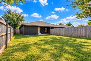 A residential backyard with a house, a wooden fence, and a grassy lawn. - NEW..Walk to UMHB & Downtown & 3BR & Pets Welcome (Belton)