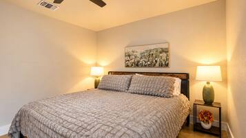 A bedroom with a bed, two bedside lamps, a ceiling fan, and a wall-mounted painting.