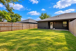 A residential backyard with a wooden fence, a house with a dark exterior, and a well-maintained lawn. - NEW..Walk to UMHB & Downtown & 3BR & Pets Welcome (Belton)
