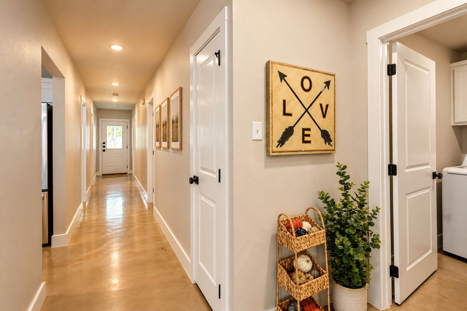 A hallway with white doors, a wall-mounted sign with 'LOVE' and arrows, a woven basket shelf with decorative items, and a potted plant.