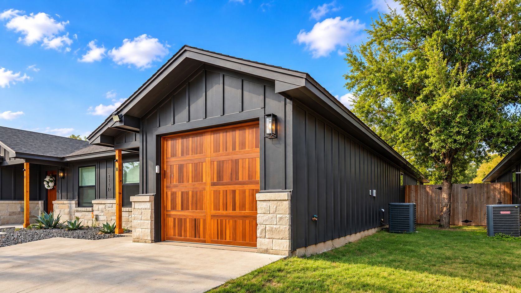 A modern house with a large garage door, stone foundation, and a well-maintained lawn.