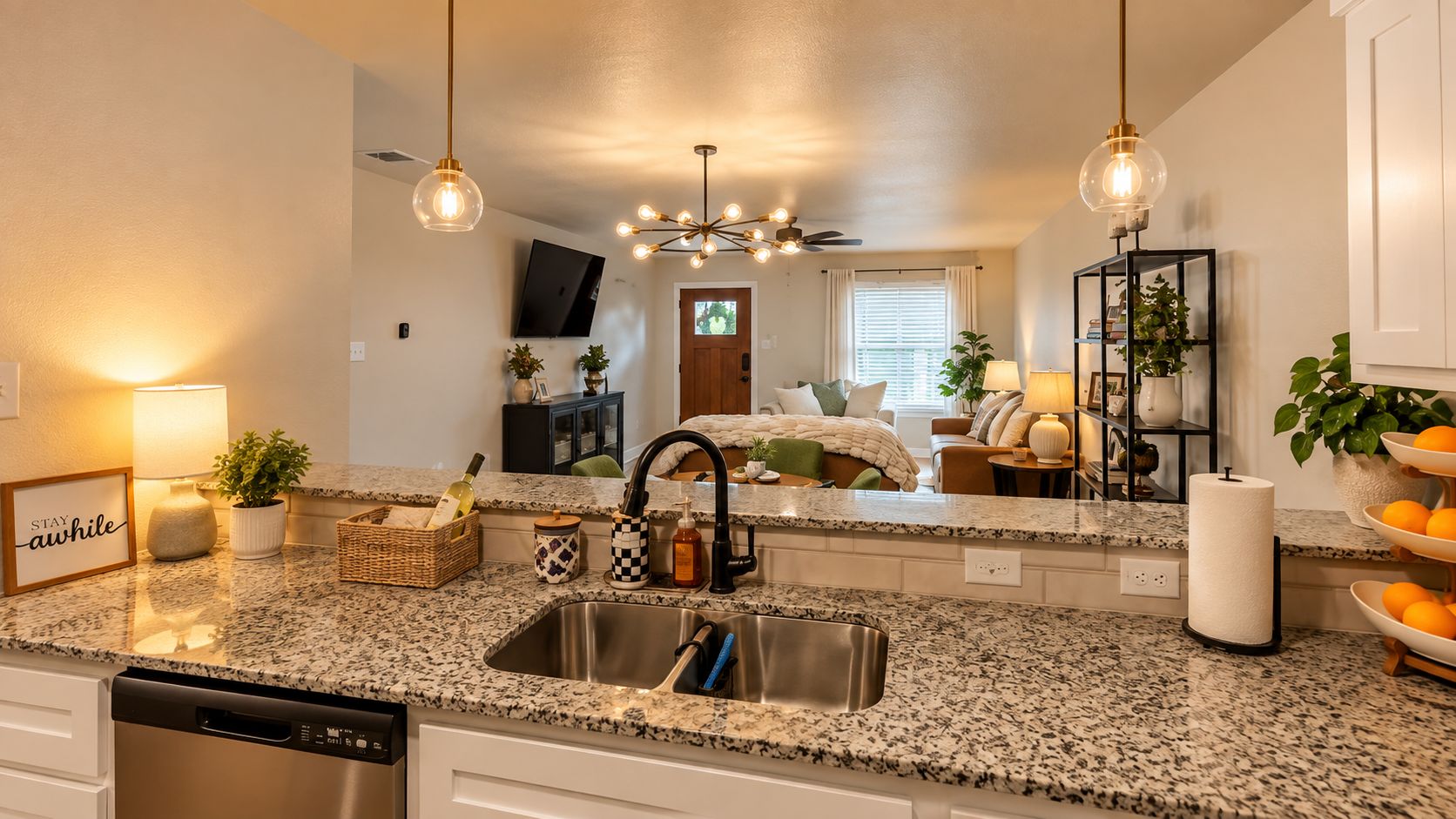 A modern kitchen with granite countertops, stainless steel sink, and pendant lighting.