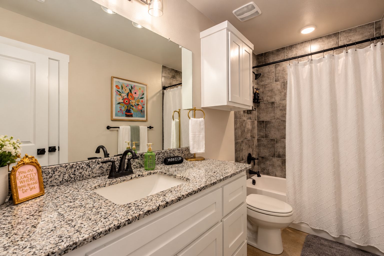 A bathroom with a granite countertop sink, a white toilet, and a shower curtain.