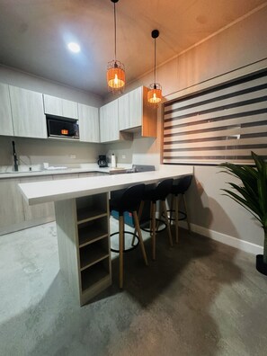 A modern kitchen with a white countertop, two hanging pendant lights, a built-in microwave, and a bar area with stools. - Premiun 1-Bed Apart in Pinilla - Tamarindo - Avellanas w AC / Pool / Rancho BBQ (Pinilla)
