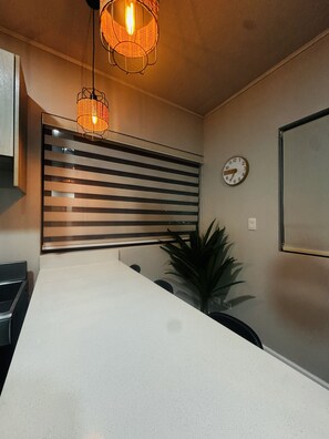 A kitchen with a white countertop, a striped panel above the sink, a clock on the wall, and a hanging light fixture. - Premiun 1-Bed Apart in Pinilla - Tamarindo - Avellanas w AC / Pool / Rancho BBQ (Pinilla)