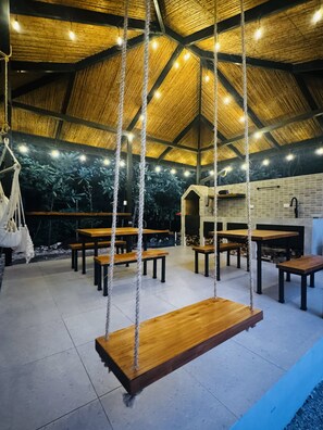 A rustic interior with wooden tables and benches, a hanging swing, and a thatched roof. - Premiun 1-Bed Apart in Pinilla - Tamarindo - Avellanas w AC / Pool / Rancho BBQ (Pinilla)
