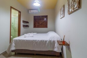 Un dormitorio con cama, aire acondicionado, puerta de madera y una pequeña mesa con una vela.