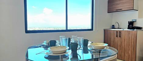 A modern kitchen with a large window, a dining table with chairs, and a coffee maker.