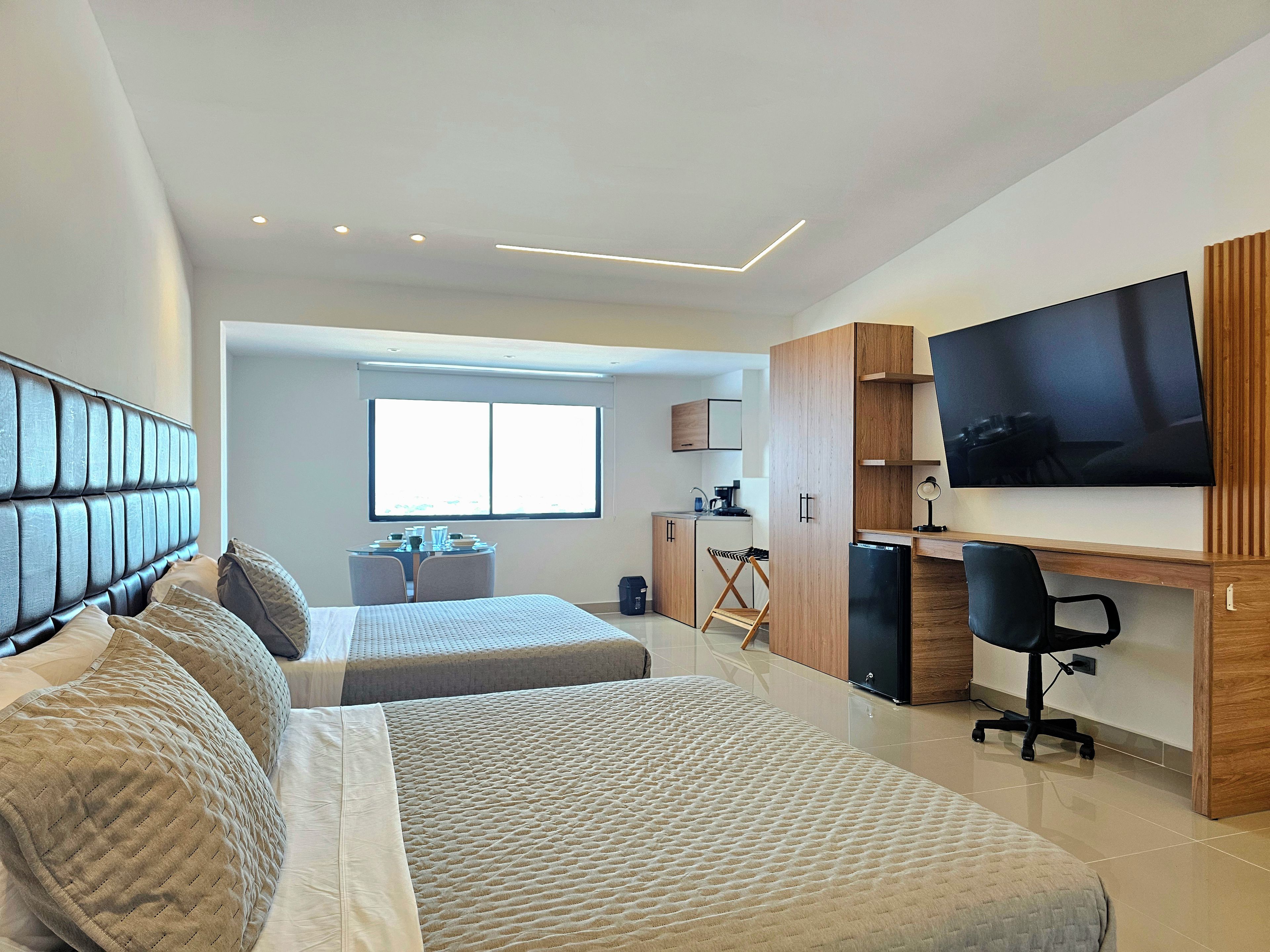 Un dormitorio moderno con dos camas, un escritorio, un televisor y una ventana.