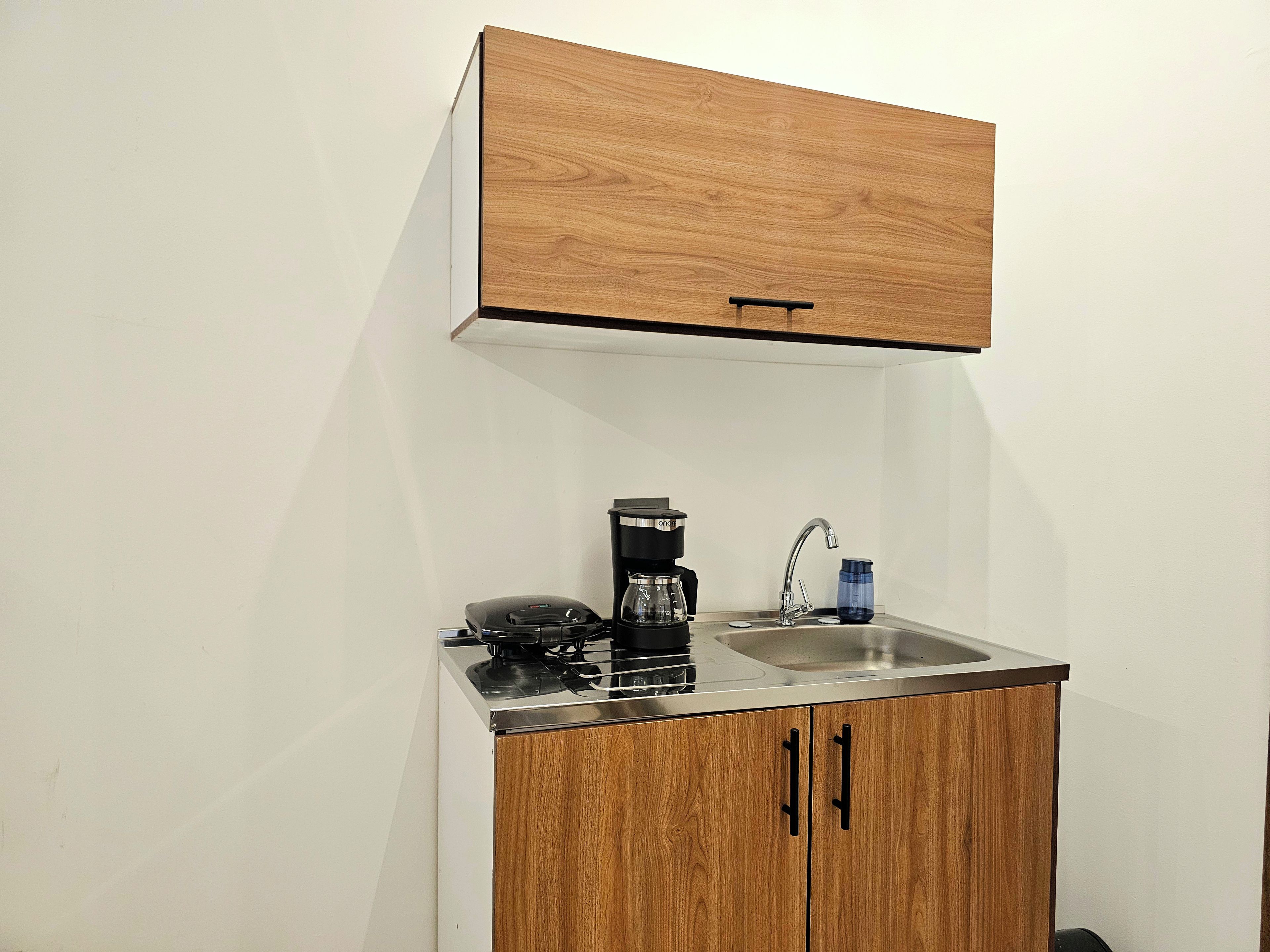 Une petite cuisine équipée avec une plaque de cuisson intégrée, une machine à café et un évier.