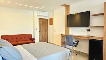 A modern hotel room with a bed, a desk, a television, and a small refrigerator.
