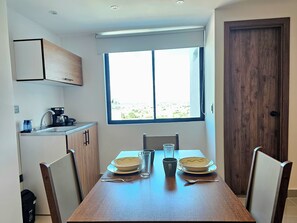 Una cocina compacta con ventana, una mesa de comedor con platos, vasos y cubiertos, y una cafetera.