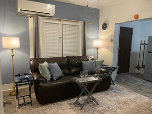 A living room with a leather sofa, two lamps, a small table with glasses, and a door in the background. - Charming Cozy Midtown Cottage near Lake Ella/FSU/FAMU/CIVIC CENTER/TMH (Tallahassee)