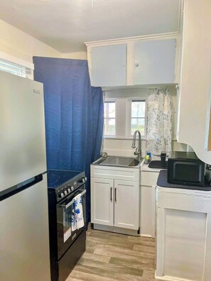 A compact kitchen with a refrigerator, stove, microwave, and sink. - Charming Cozy Midtown Cottage near Lake Ella/FSU/FAMU/CIVIC CENTER/TMH (Tallahassee)