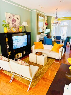 Una sala de estar con televisor, sofá, reposapiés y un comedor con sillas.