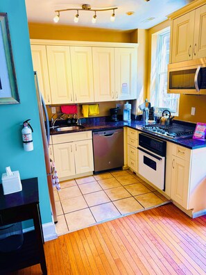 Una cocina con armarios de tonos claros, un refrigerador de acero inoxidable, una cafetera y un hervidor sobre la encimera.