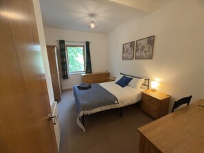 A bedroom with a bed, bedside table, lamp, and a window with curtains. - Stylish and modern Oxford City Centre apartment. (Oxford)