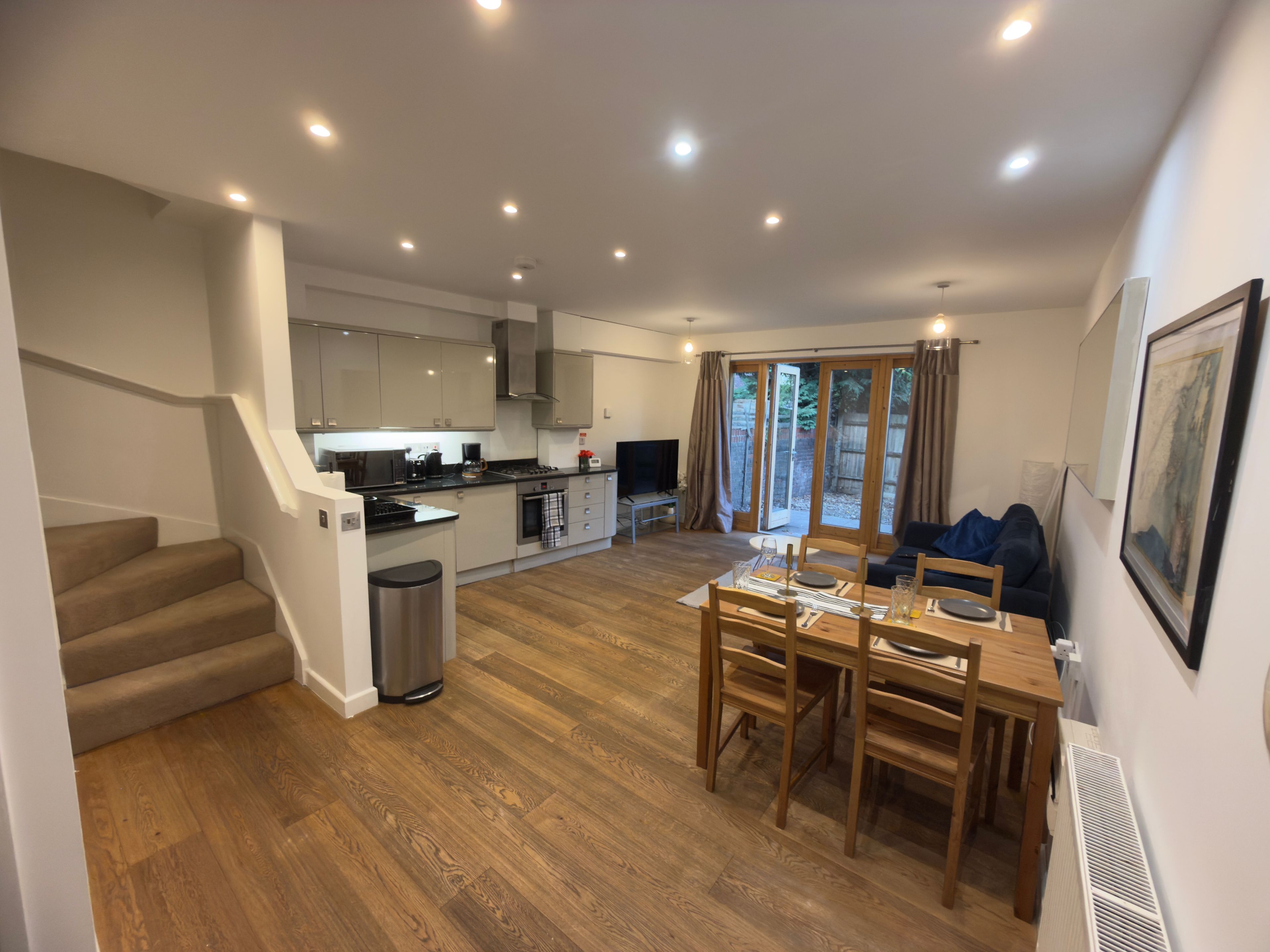 A modern kitchen with a dining area, wooden flooring, and a staircase leading to another level.