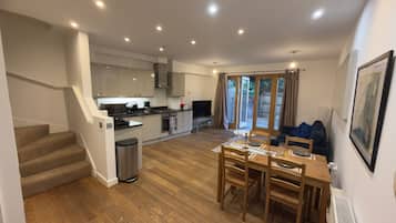 A modern kitchen with a dining area, wooden flooring, and a staircase leading to another level.