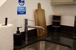 A kitchen sink with a faucet, a soap dispenser, a wooden cutting board, and a sign instructing to wash hands. - Stylish and modern Oxford City Centre apartment. (Oxford)