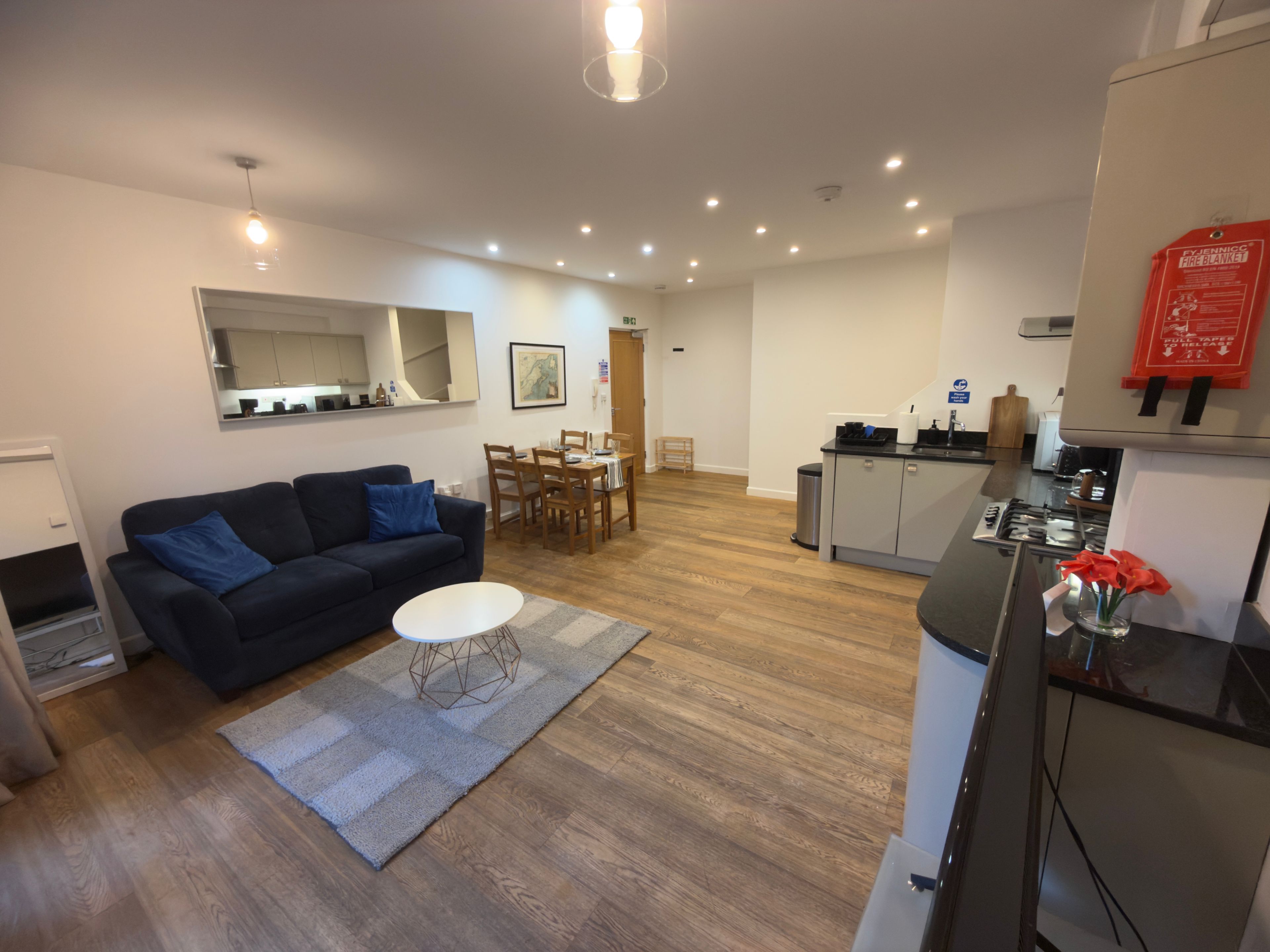 A modern living room with a sofa, a dining table, and a kitchen area with a refrigerator and stove.