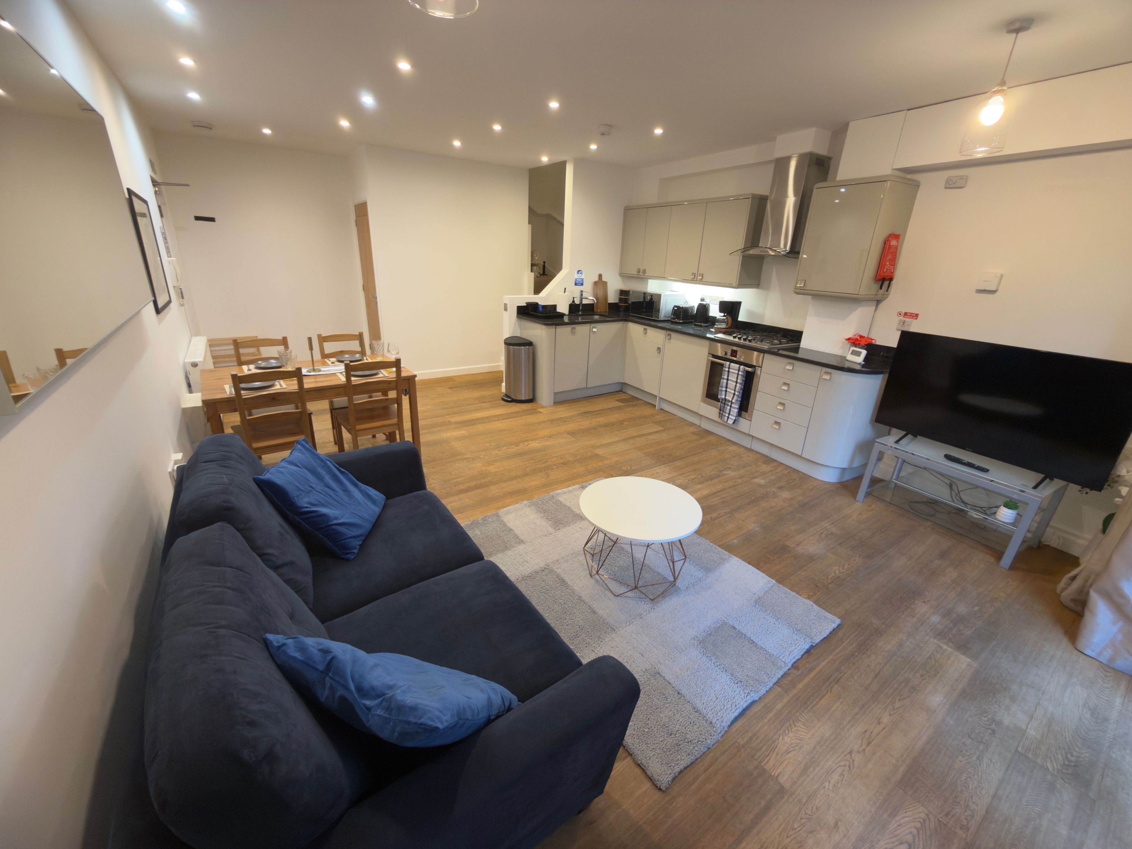 A modern living room with a sofa, a dining table, and a kitchen area with a stove and a TV.