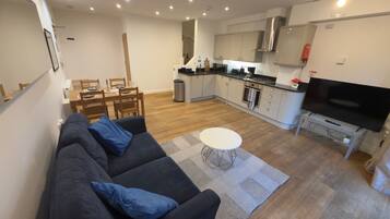 A modern living room with a sofa, a dining table, and a kitchen area with a stove and a TV.