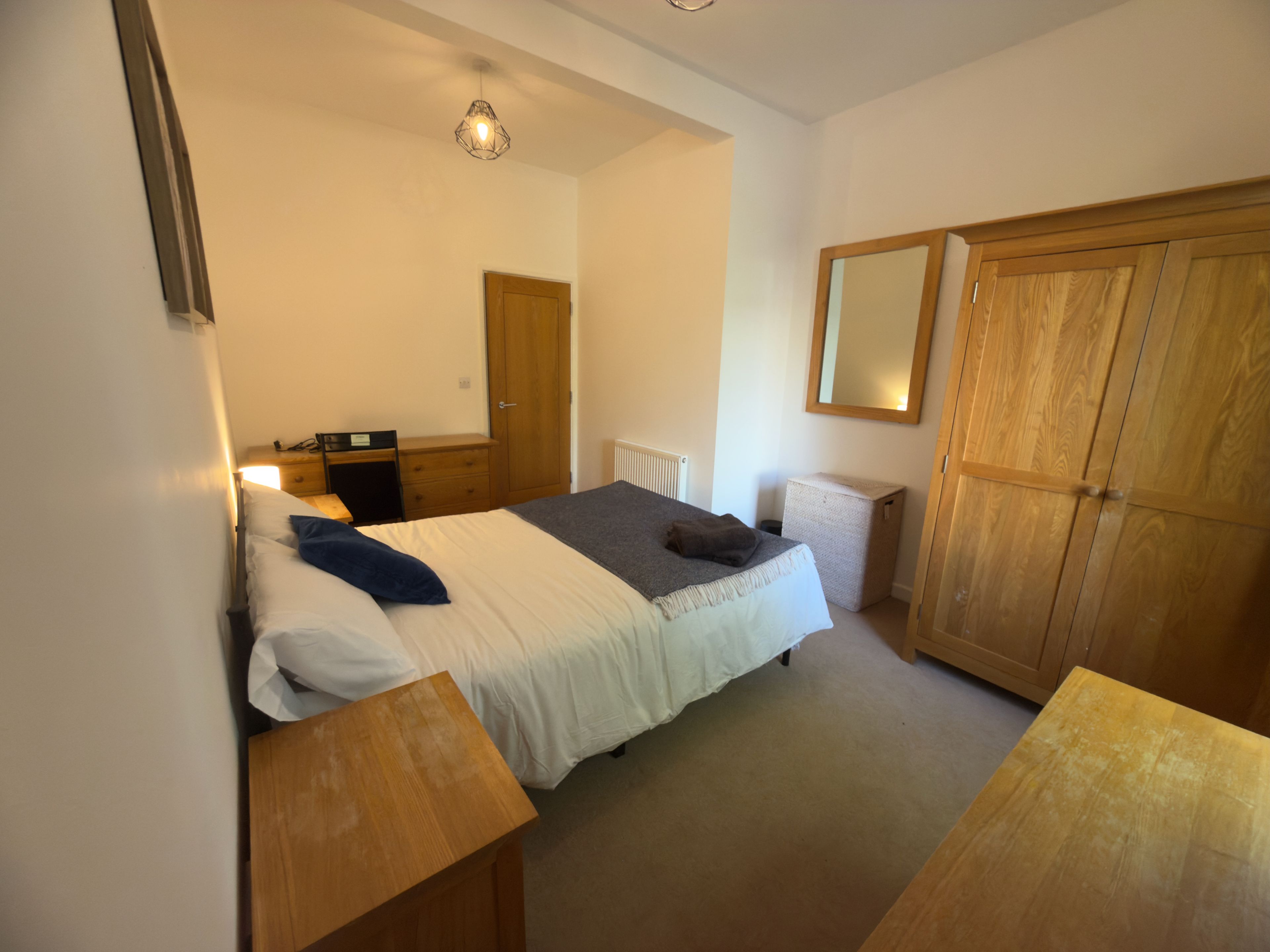 A bedroom with a bed, bedside tables, a wardrobe, a mirror, and a radiator.