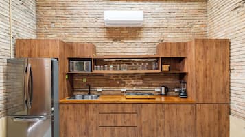 Una cocina compacta con gabinetes de madera, un refrigerador de acero inoxidable, un microondas, un lavamanos y una estufa integrada.