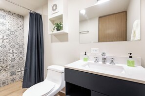 A bathroom with a white toilet, a black shower curtain, a white sink with two soap dispensers, and a mirror above the sink. - Hacienda Tapia (Monterrey)