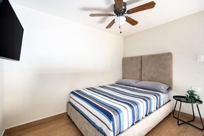 A bedroom with a bed, a ceiling fan, a small table with a plant, and a wall-mounted TV. - Hacienda Tapia (Monterrey)