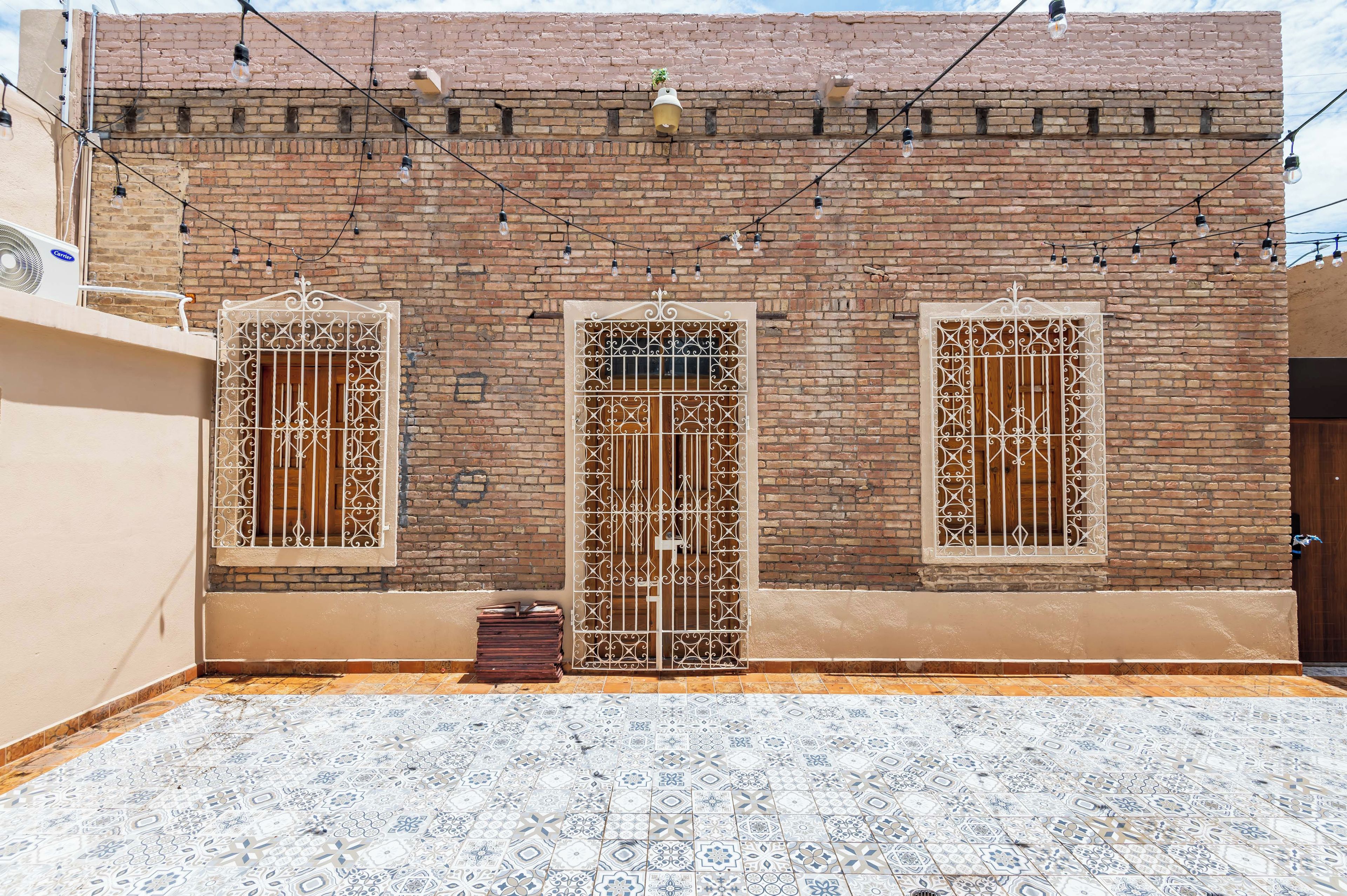 A building with three windows, each with decorative metal grilles, and a tiled courtyard.