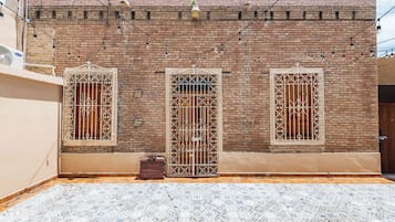 A building with three windows, each with decorative metal grilles, and a tiled courtyard.