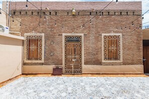 Un edificio con tres ventanas, cada una con rejas decorativas de metal, y un patio empavedado.