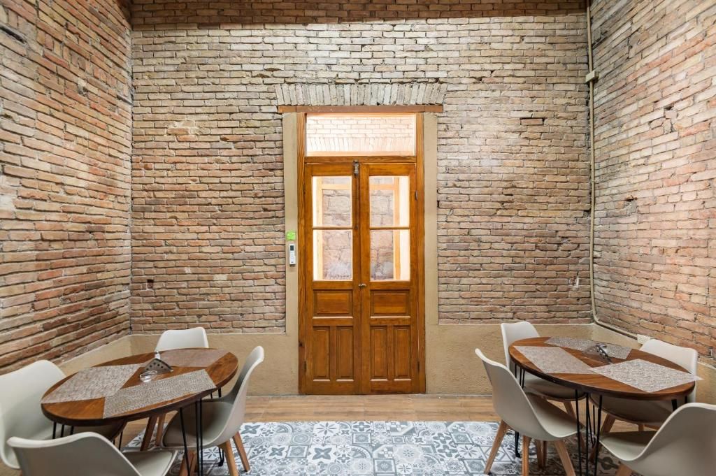 Una habitación con pared de ladrillo, puerta de madera y una mesa redonda con sillas.