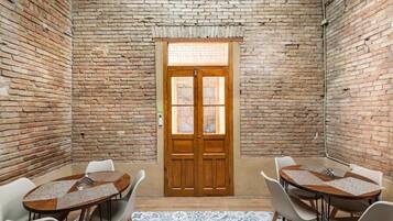 Una habitación con pared de ladrillo, puerta de madera y una mesa redonda con sillas.