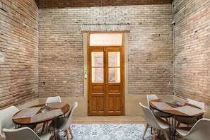Une pièce avec un mur en briques, une porte en bois et une table ronde entourée de chaises.