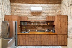 Cocina compacta con armarios de madera, refrigerador de acero inoxidable, microondas y cafetera.