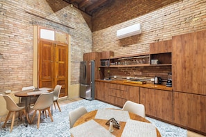 Una cocina con armarios de madera, un refrigerador de acero inoxidable y una zona de comedor con mesa y sillas.