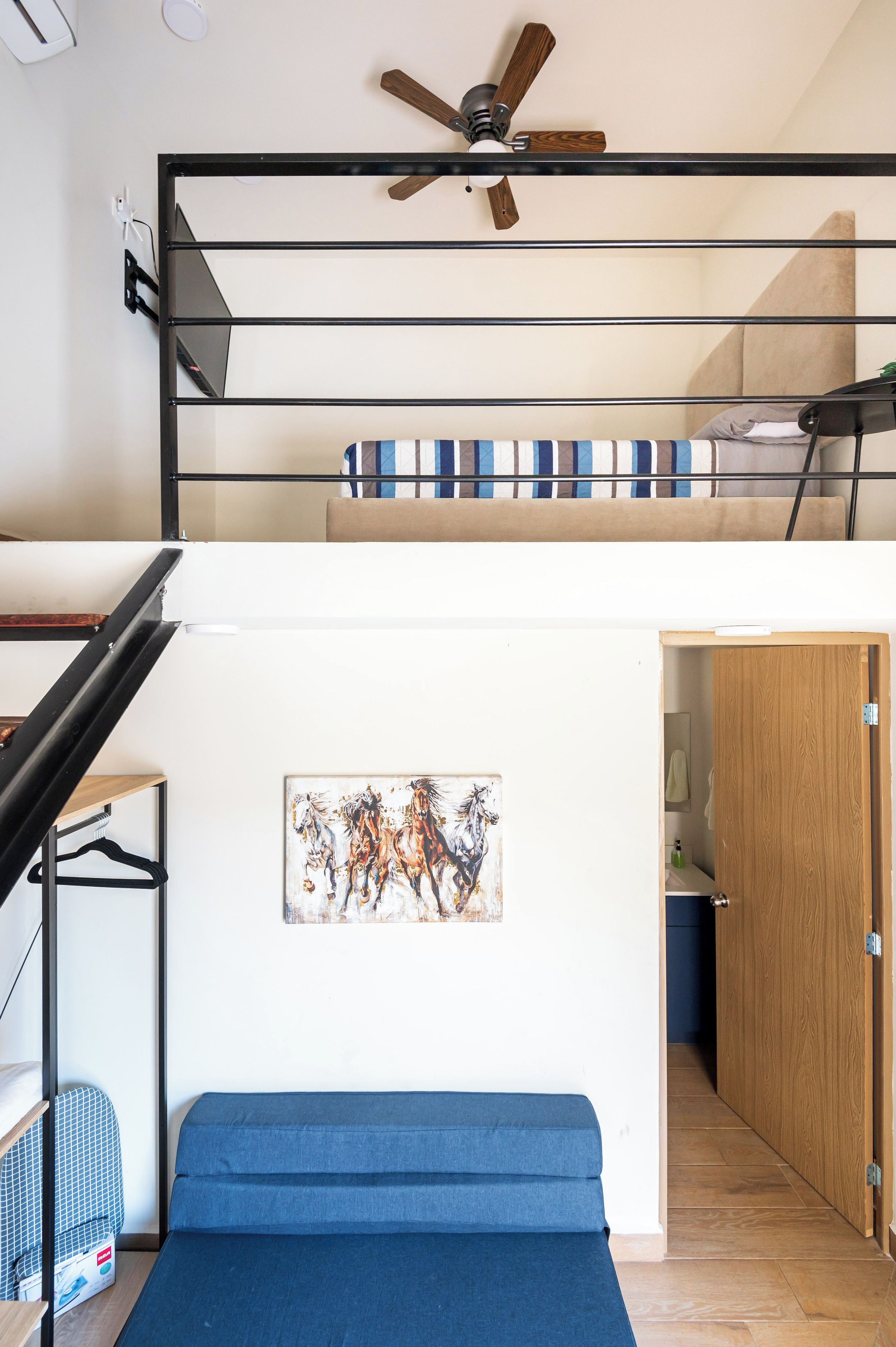 A multi-level interior with a staircase, a ceiling fan, a painting, and a blue sofa.