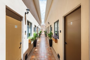 Pasillo con puertas numeradas 15 y 6, flanqueado por plantas en macetas y equipado con lámparas de pared.
