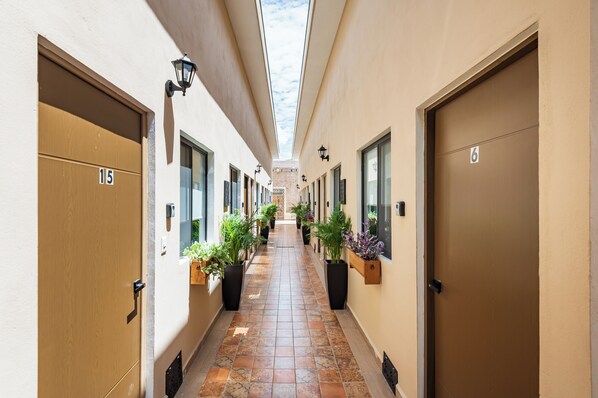 A corridor with doors numbered 15 and 6, flanked by potted plants and equipped with wall-mounted lamps. - Hacienda Tapia (Monterrey)