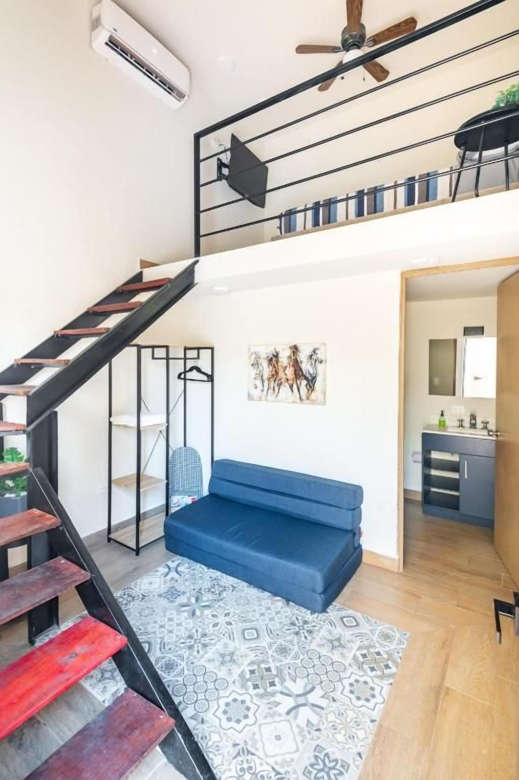 Un interior moderno con una escalera, un sofá azul, una alfombra estampada y una zona de cocina.