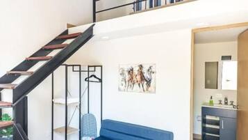 Un interior moderno con una escalera, un sofá azul, una alfombra estampada y una zona de cocina.