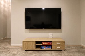 Un téléviseur à écran plat fixé au mur, au-dessus d’un meuble de rangement en bois doté de deux tiroirs et d’une étagère.