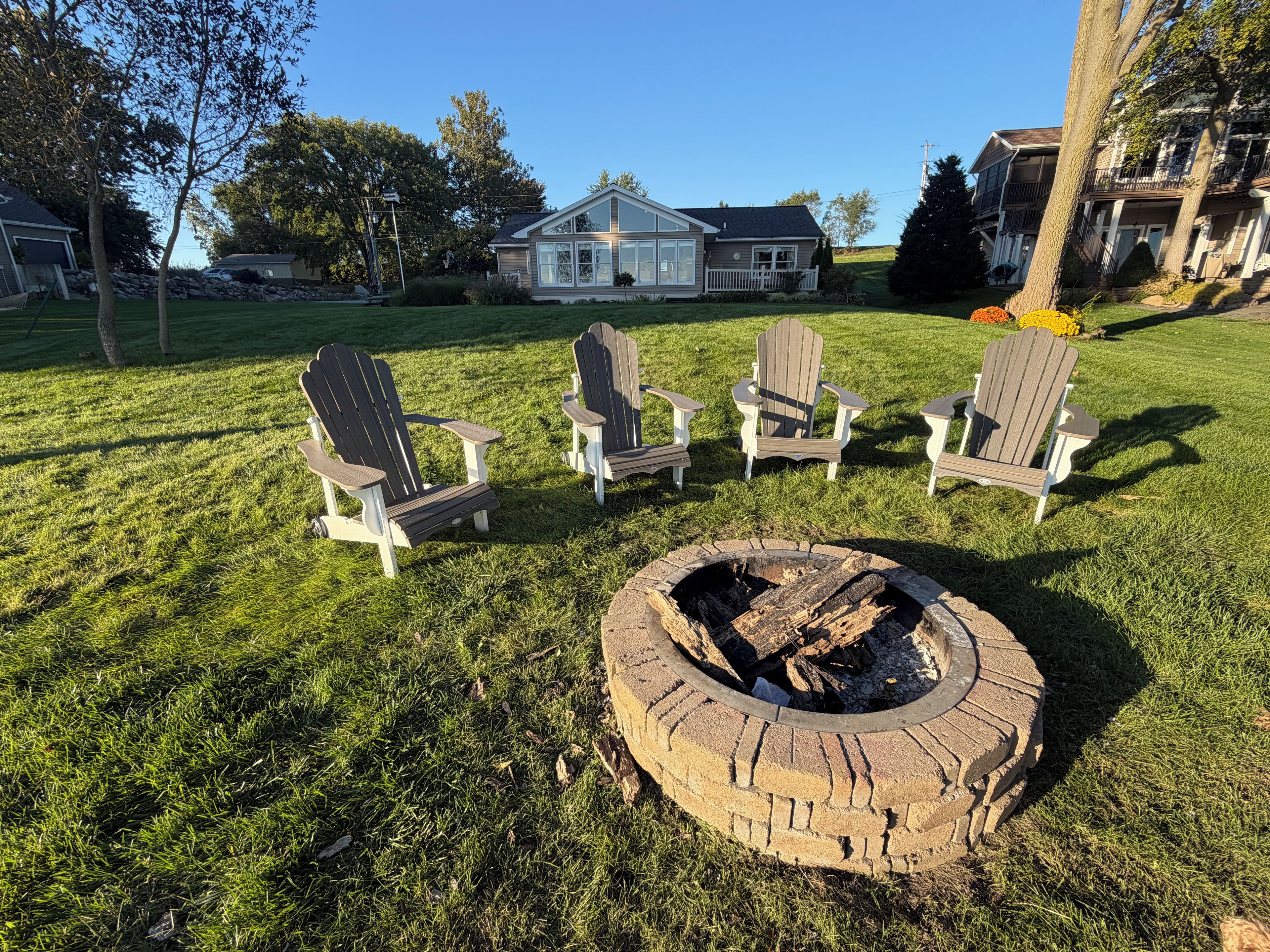 A grassy outdoor area with a fire pit and four Adirondack chairs.