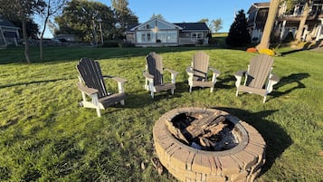 A grassy outdoor area with a fire pit and four Adirondack chairs.