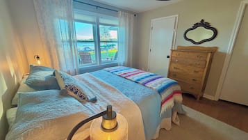 Een slaapkamer met een bed, een dressoir, een raam met gordijnen en een lamp.