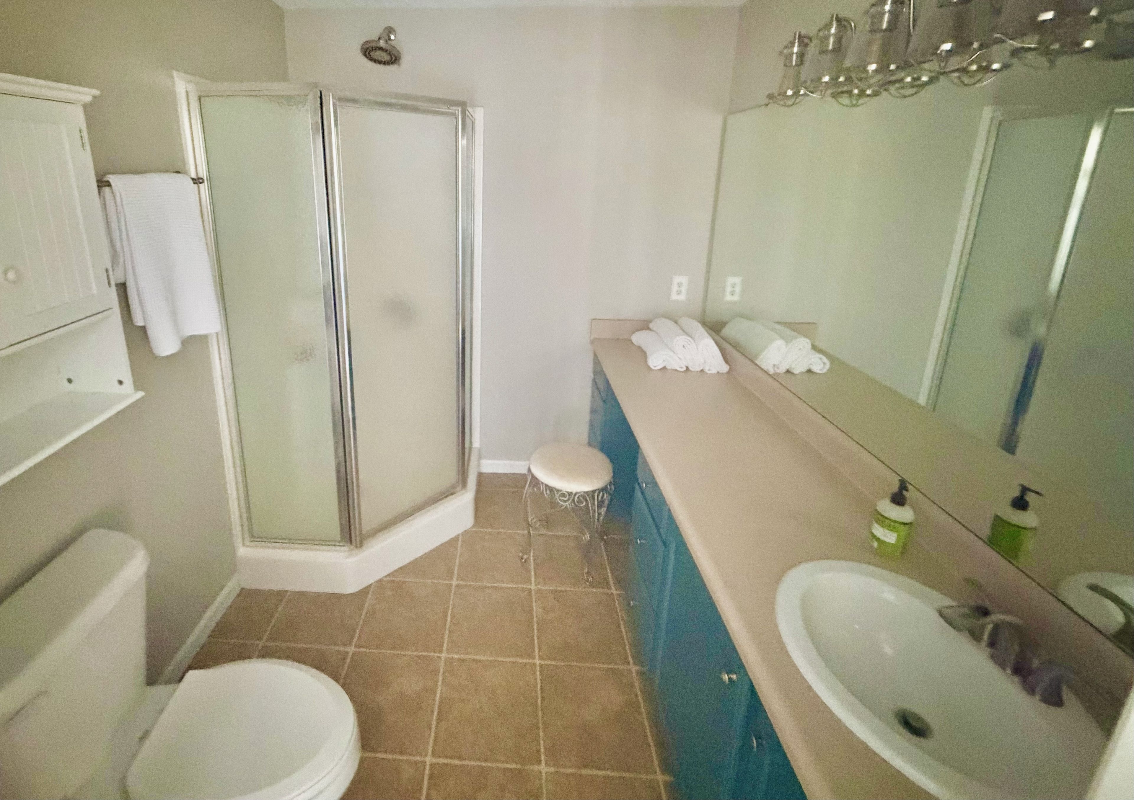 A bathroom with a glass shower enclosure, a toilet, a sink, and a vanity with towels.