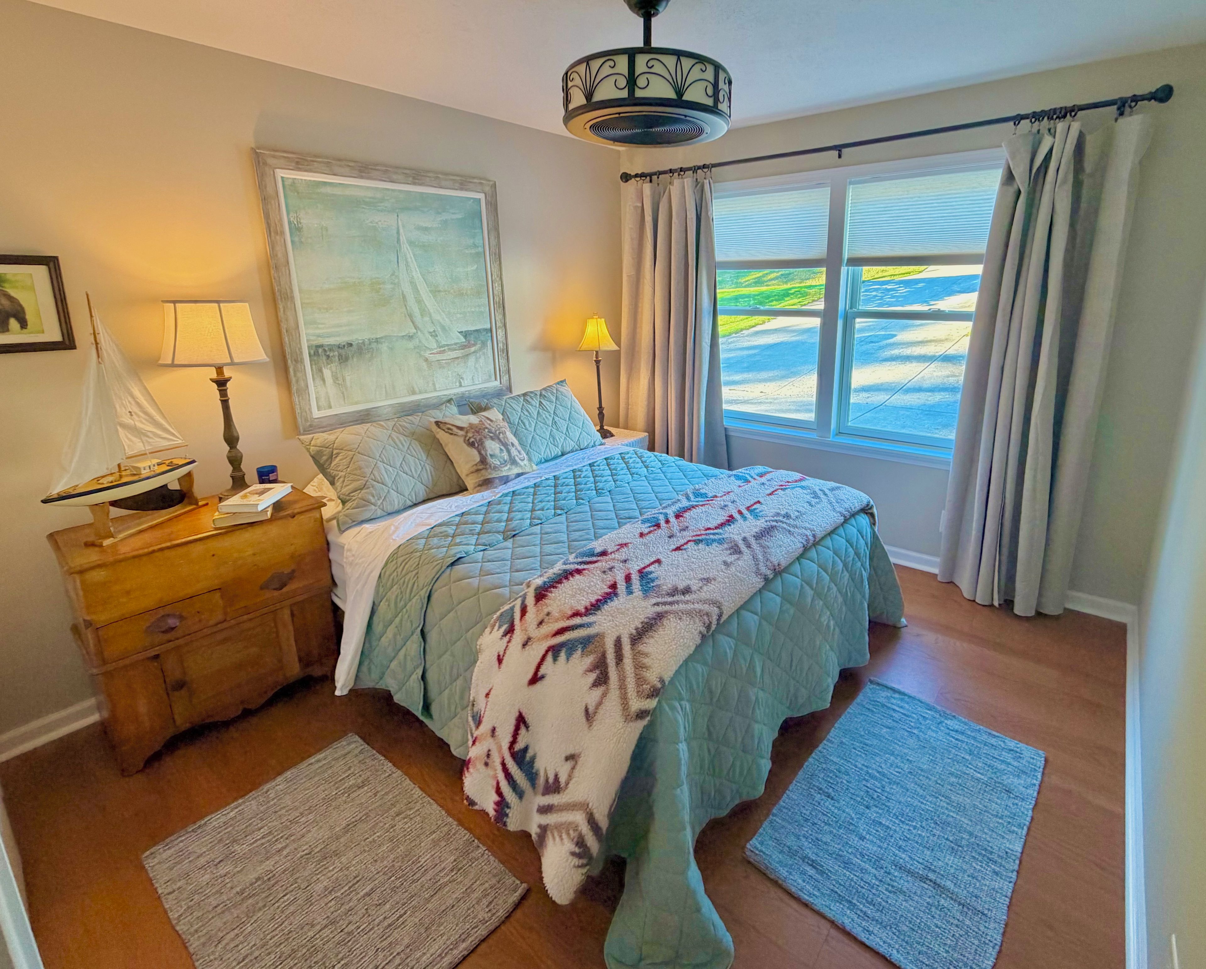 Een slaapkamer met een bed, nachtkastje, lamp, schilderij en uitzicht op de omgeving.